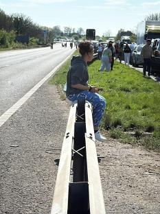 Woman sitting on a highway barrier, traffic jam in the background.