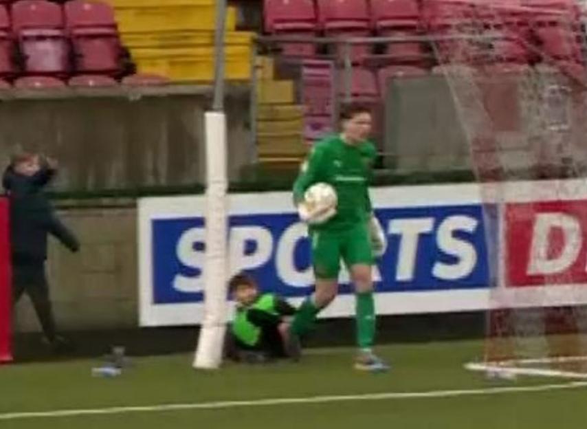 Soccer goalie standing near a young child sitting on the ground.