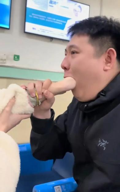 Video still of a woman's hand stuck in a man's mouth in a hospital waiting room.