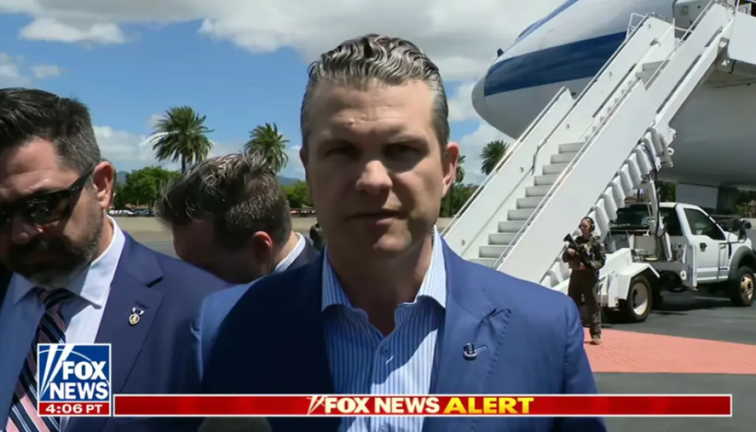 Man in suit being interviewed near an airplane.