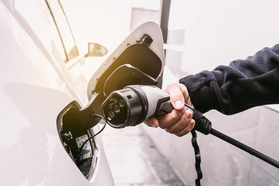 Hand plugging charging cable into electric car.