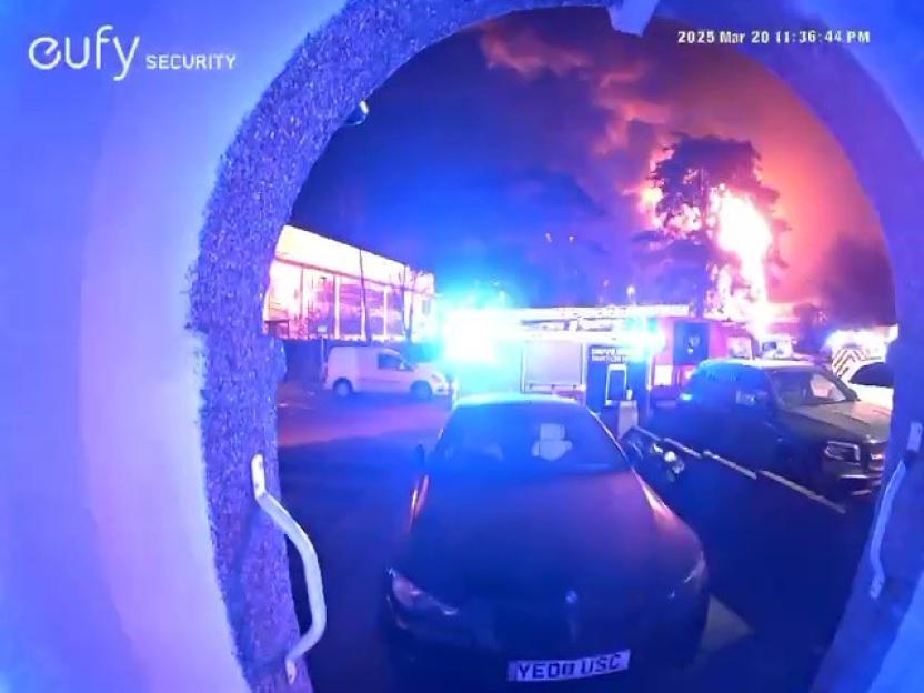 Nighttime security camera footage of a large fire with emergency vehicles responding.