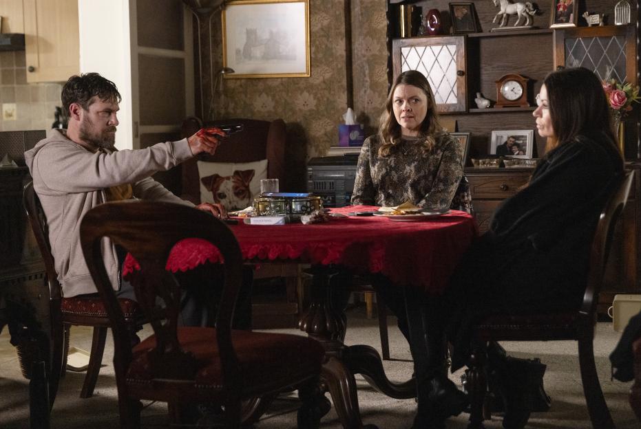 A man points a gun at two women sitting at a table.