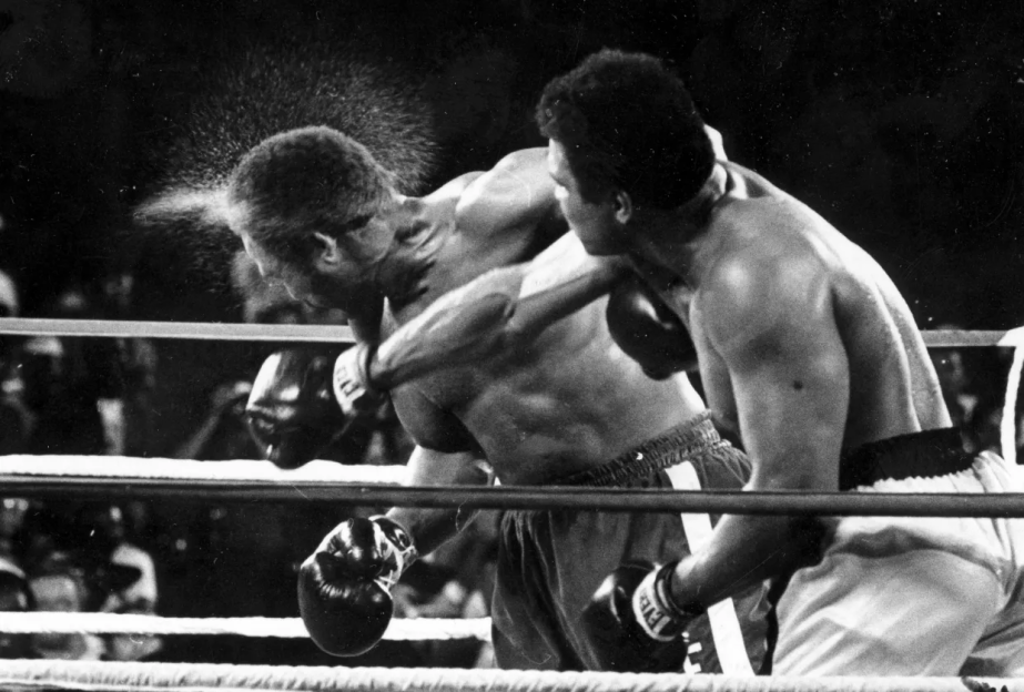 Black and white photo of two boxers in the ring, one throwing a punch.