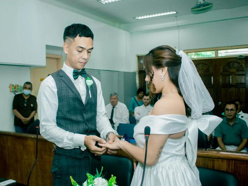 A wedding ceremony. A man places a ring on a woman's finger.