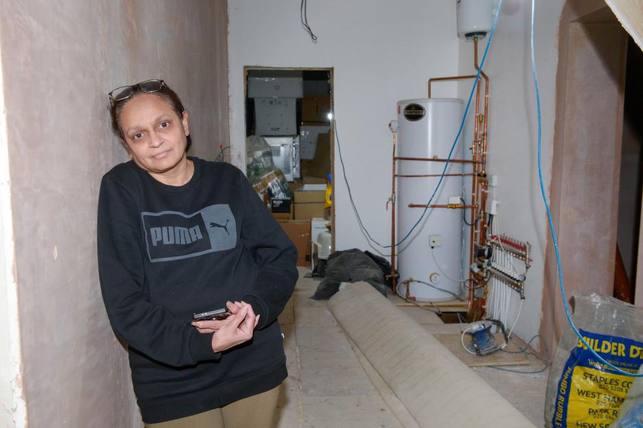 Woman in a Puma sweatshirt stands in a hallway of an unfinished home.