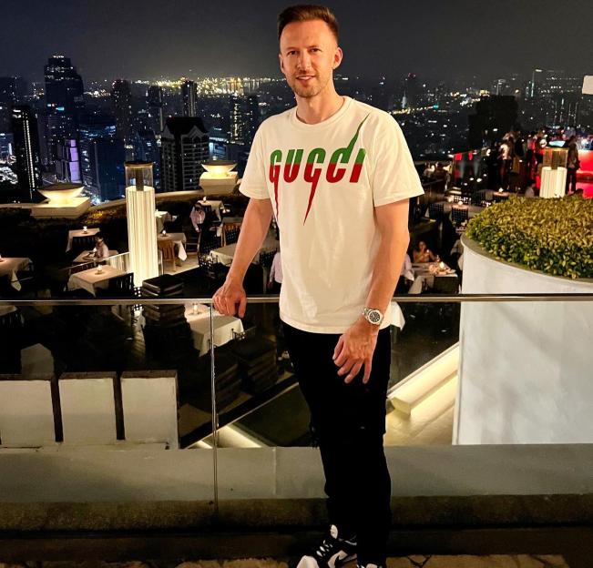 a man wearing a gucci shirt stands on a balcony