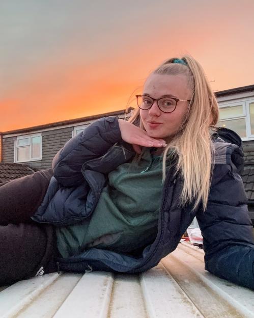 Young woman lying on a van roof at sunset.