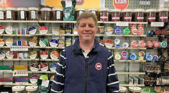 Man standing in front of shelves stocked with tobacco products.