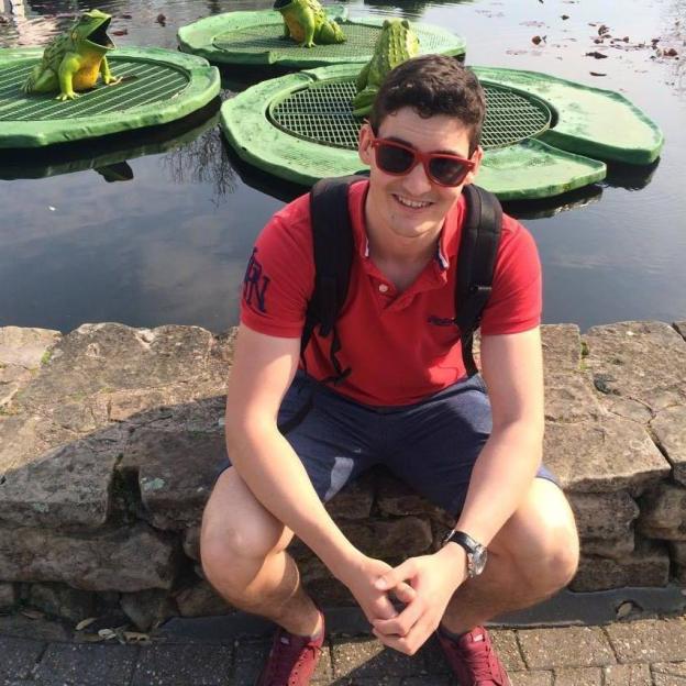 A man sits on a stone wall by a pond with frog statues.