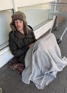 Homeless man sitting on the ground wrapped in a blanket.