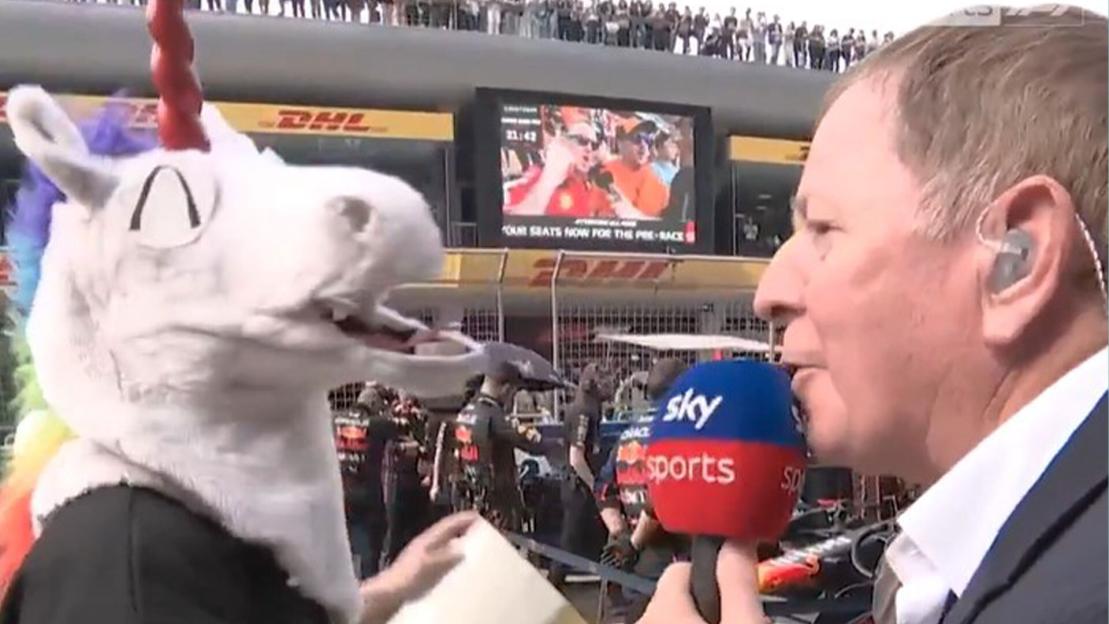 A reporter interviews a person in a unicorn costume at a race track.