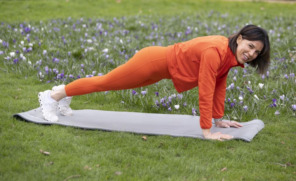 Woman in orange athletic wear doing a plank exercise outdoors.