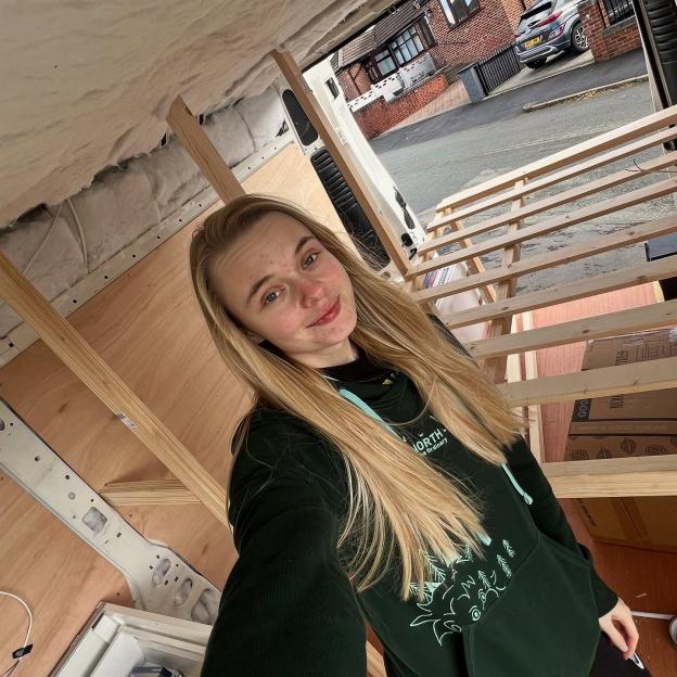 Young woman in van conversion, building a bed frame.