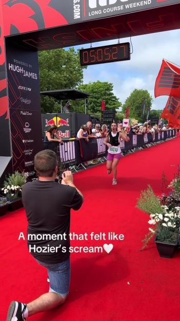 A woman finishes a race, a man kneels to take a photo.