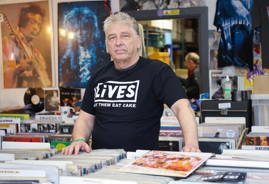 Shop owner standing behind a counter full of vinyl records.