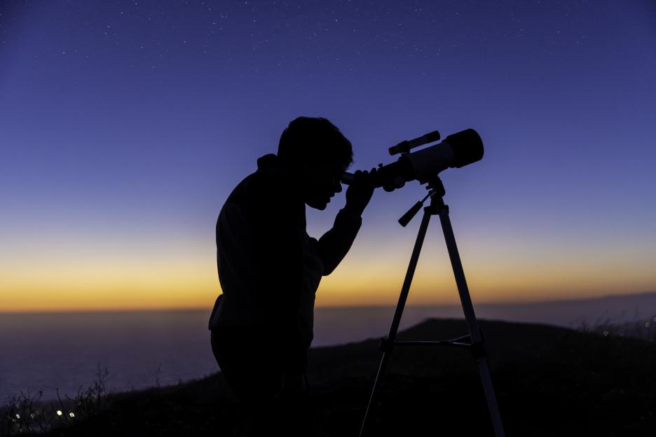 Silhouette of a boy using a telescope at sunset.