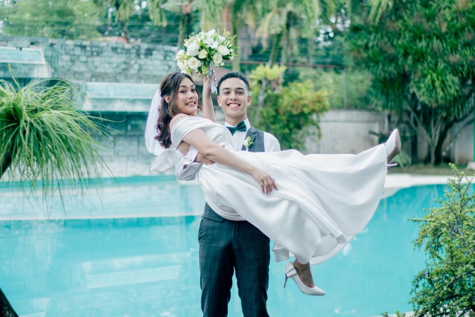 Groom carrying bride near a pool.