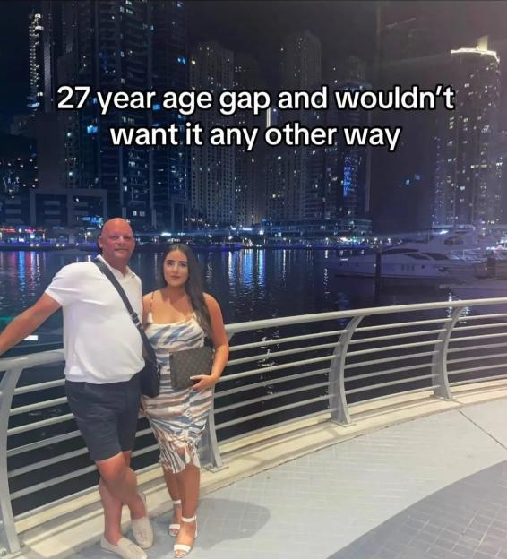 Couple with a 27-year age gap posing at night by a waterfront.