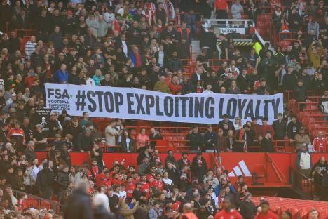 Fans holding a banner that reads "#STOP EXPLOITING LOYALTY" at a soccer match.