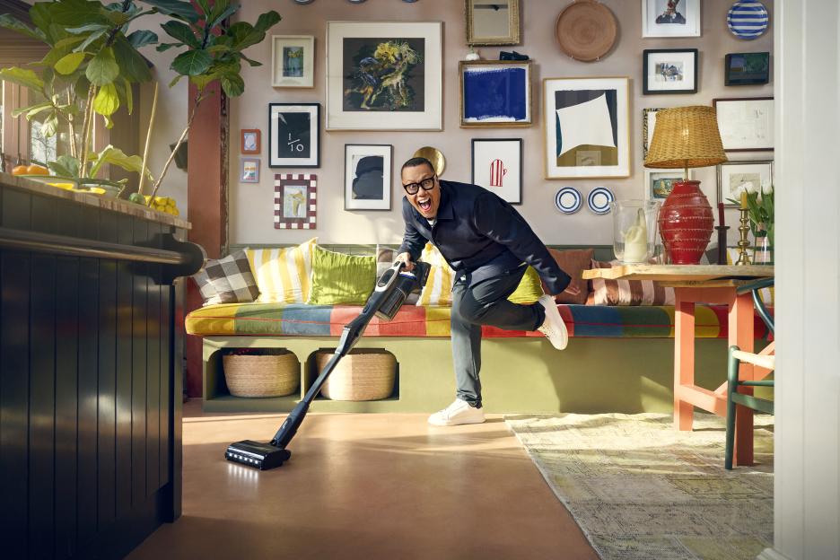 A man playfully vacuums in a brightly colored room.