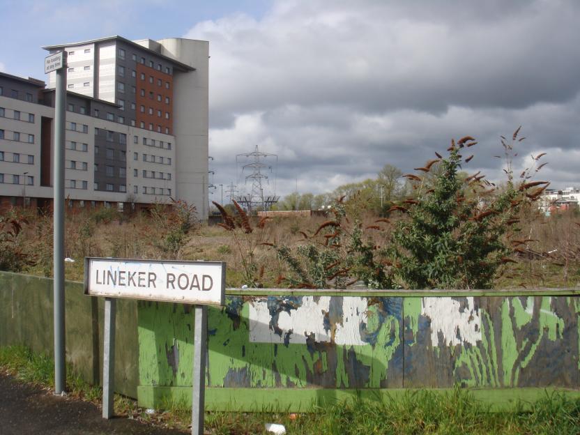 Lineker Road sign in front of a dilapidated fence and a modern apartment building.