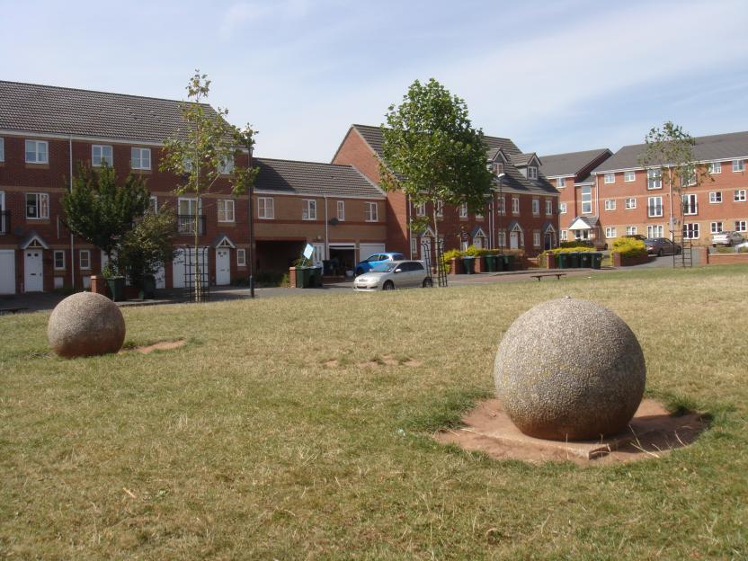 Two large stone spheres in a grassy area in front of modern brick townhouses.