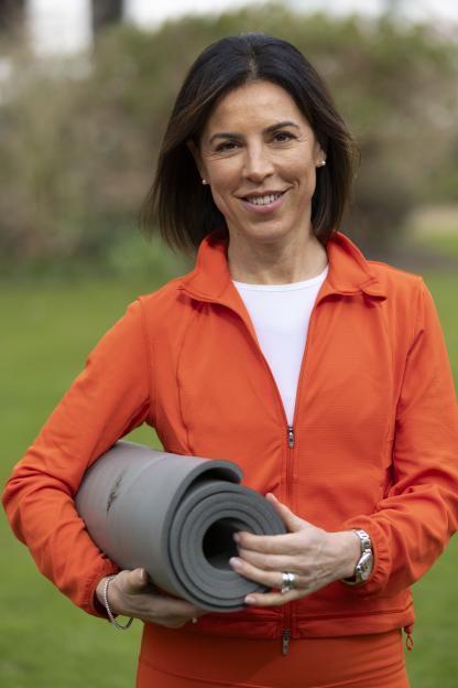 Woman in orange jacket holding a rolled-up yoga mat.