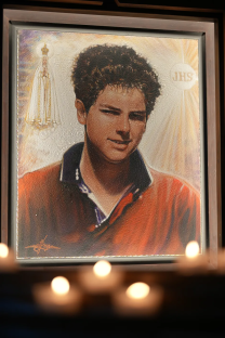 Portrait of a young man in a red shirt, with a depiction of the Virgin Mary in the background.