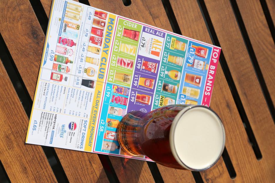 Pint of beer on a pub table next to a drinks menu.