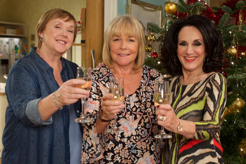 Three women toasting with champagne flutes in front of a Christmas tree.