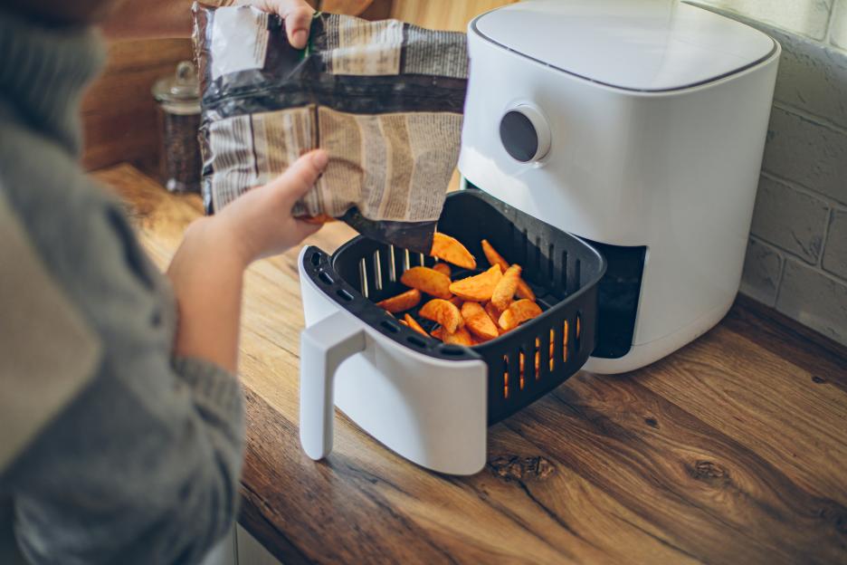 Woman putting potato wedges into an air fryer.