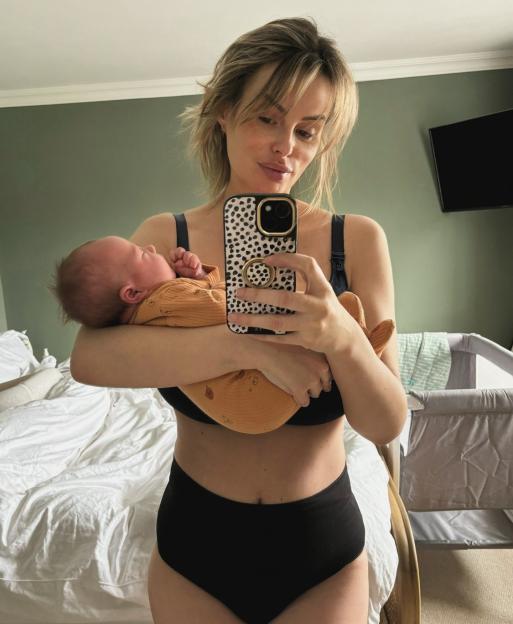 A woman holding her newborn baby and taking a selfie.