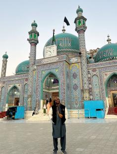 Person standing in front of a teal and blue mosque.