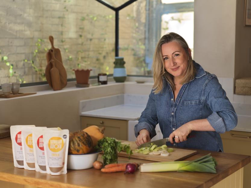 Woman chopping vegetables in a kitchen, with packages of Borough Broth bone broth on the counter.