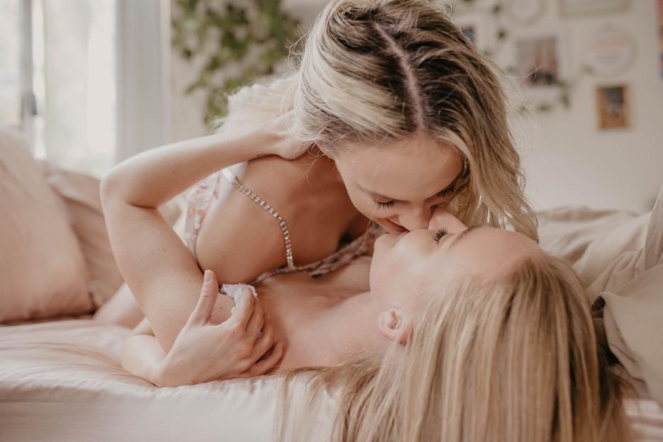 Two women kissing on a bed.