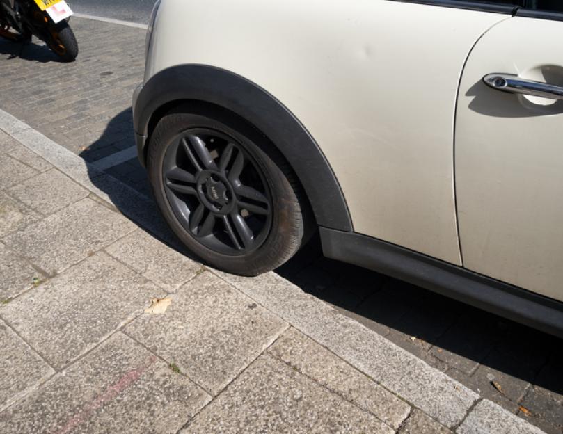 Badly parked car with one wheel on the pavement.