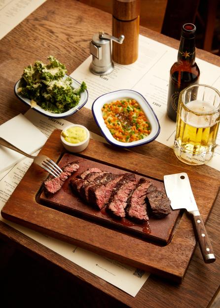 Sliced steak on a hot stone, served with sides and beer.