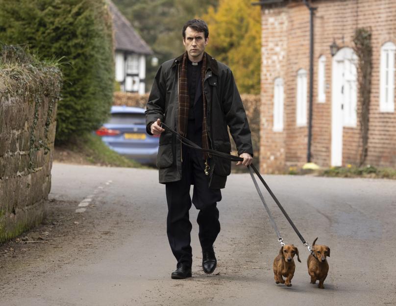 Matthew Lewis, actor known for playing Neville Longbottom in the Harry Potter films, walking two dachshunds on set of the TV drama *Murder Before Evensong*.