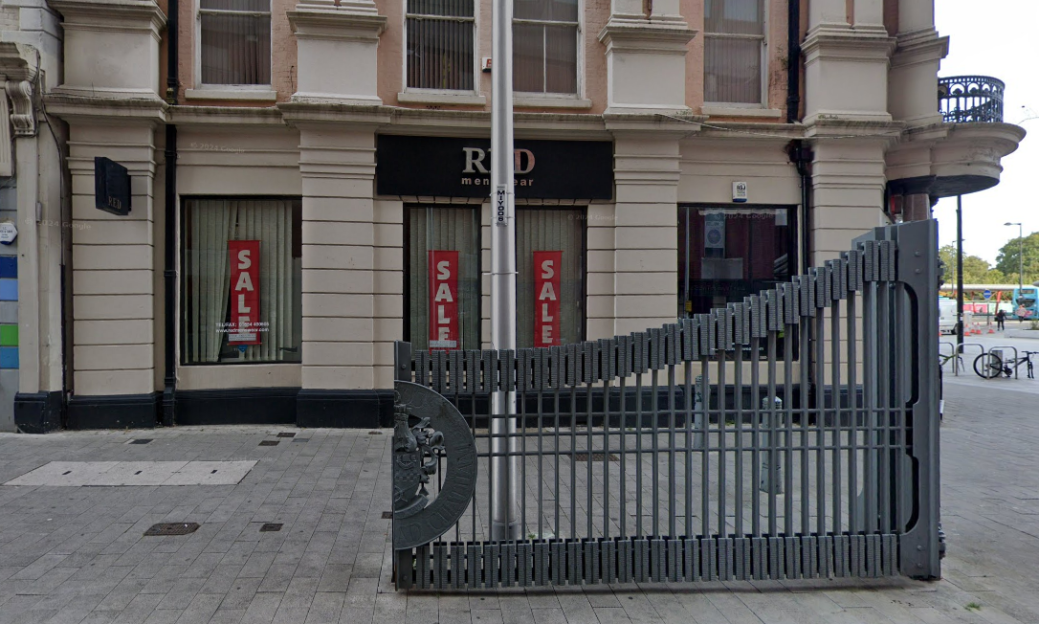 R&D menswear store with sale signs in the windows, partially obscured by a decorative gate.