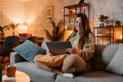 Smiling young woman relaxing on a couch at home, using a tablet.