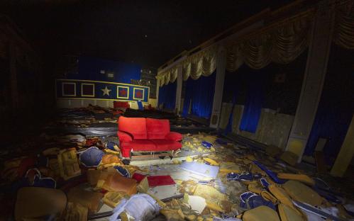 Abandoned movie theater in Thailand with a red couch and debris on the floor.
