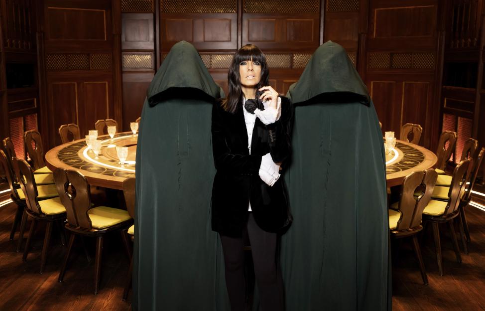 Claudia Winkleman standing between two figures in hooded cloaks.