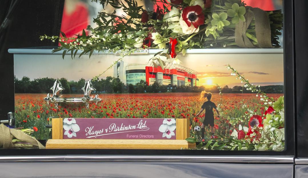 Hearse with a child's coffin decorated with flowers and a photo of a soccer field and stadium.