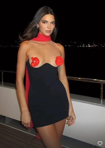 Kendall Jenner on a yacht wearing a short black dress with red accents.