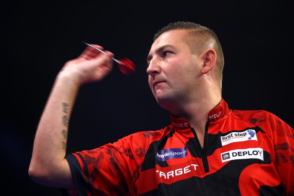 Nathan Aspinall throwing a dart during a darts match.