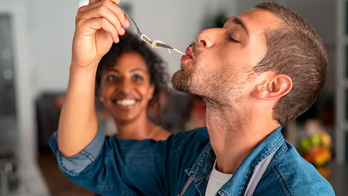 Man being fed spaghetti by a woman.