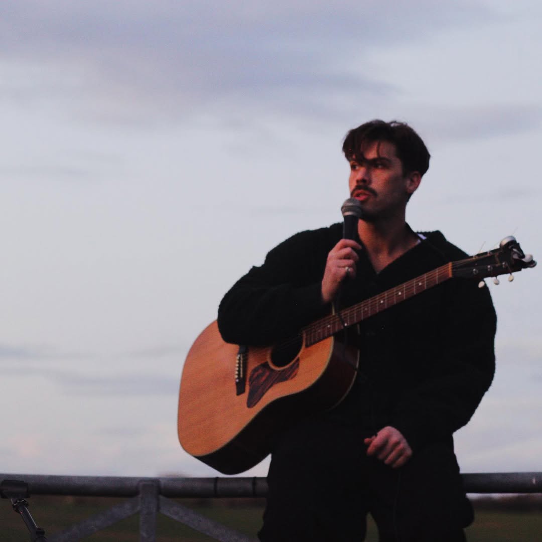 Aiden Grimshaw singing and playing an acoustic guitar.