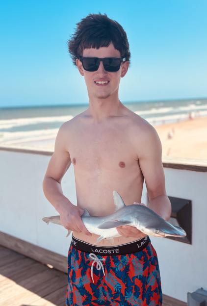 Teenager holding a small hammerhead shark on a pier.