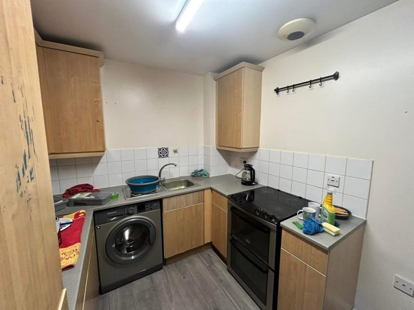 A small kitchen with light wood cabinets, a washing machine, and an electric stove.